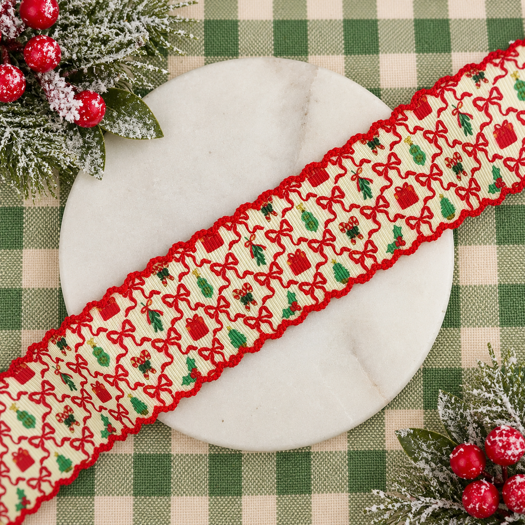 A festive moonstitch scalloped ribbon with a red scalloped border and a cream background featuring red bows, green holly, and red gift motifs, laid diagonally across a round white marble plate on a green and beige checkered tablecloth with holiday greenery and red berries.