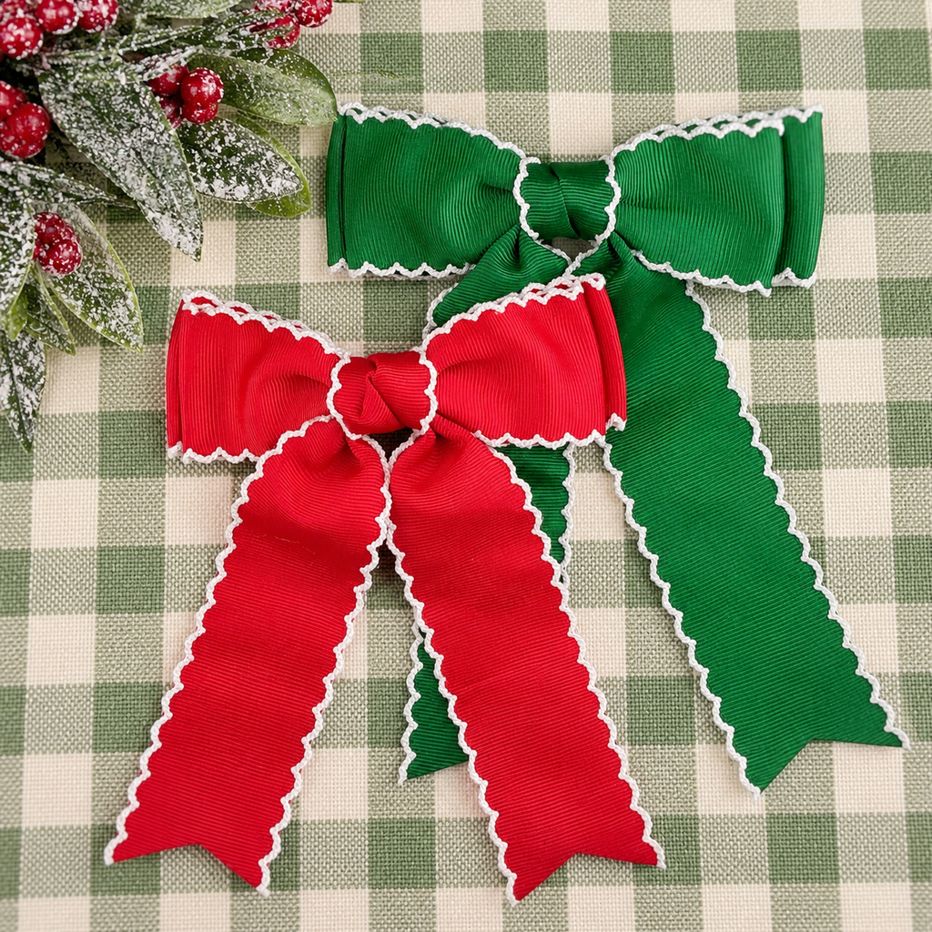 Two ribbon bows, one green and one red, both with white scalloped edges, arranged on a green and white checkered fabric background with a small decorative wreath in the corner.