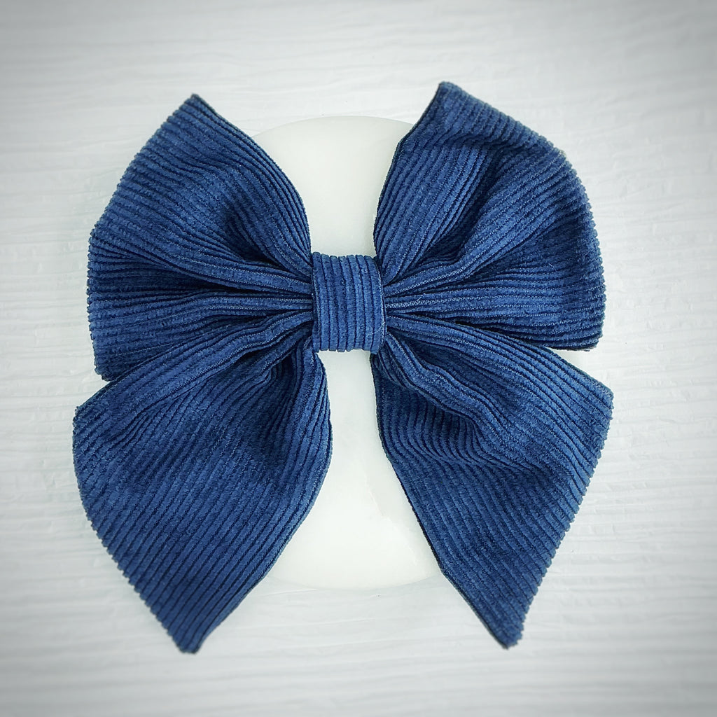 A large blue ribbed fabric bow displayed on a white mannequin head against a light gray textured background.