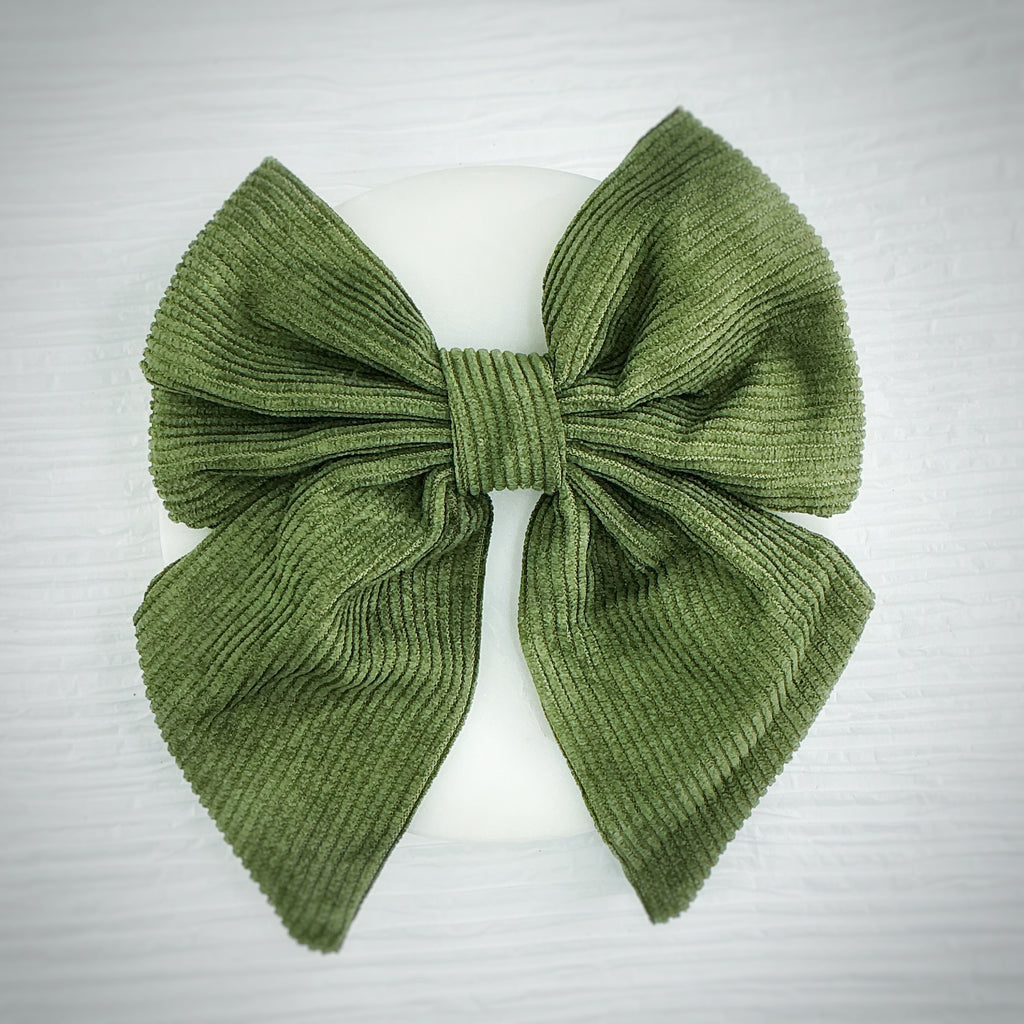 An olive green ribbed fabric bow displayed on a white mannequin head against a light gray textured background.